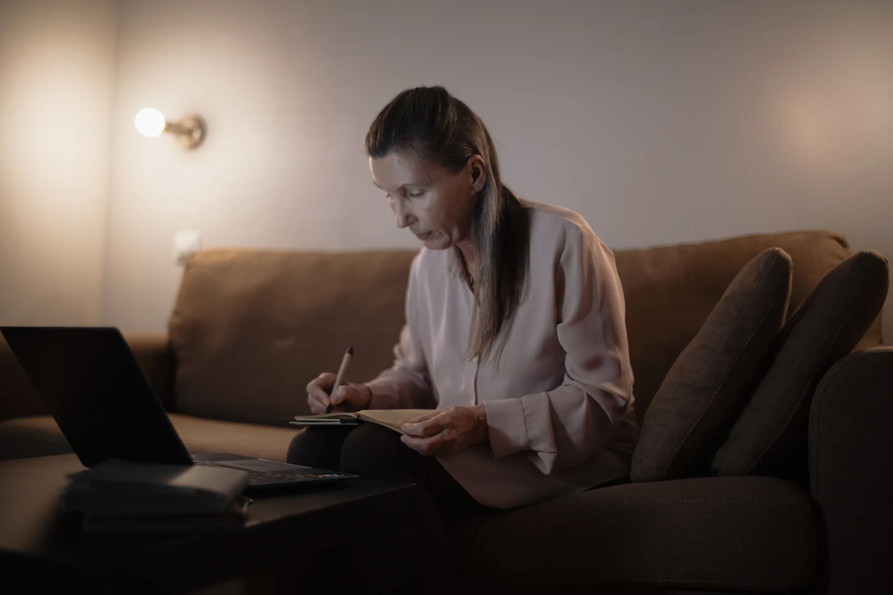 Older woman using a laptop and taking notes at home